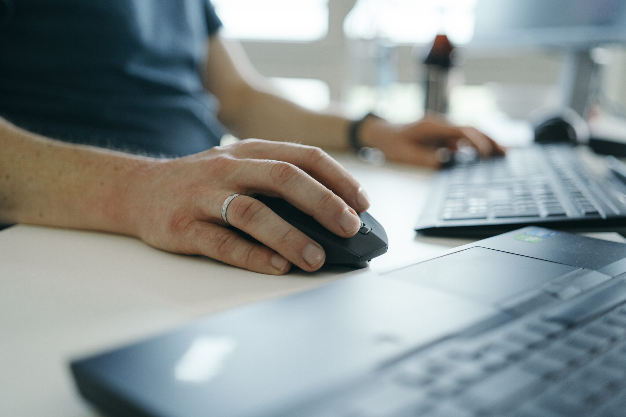 Eine Person, die einen Ehering trägt, benutzt mit der rechten Hand eine Computermaus, während sie mit der linken Hand auf einer Tastatur tippt.