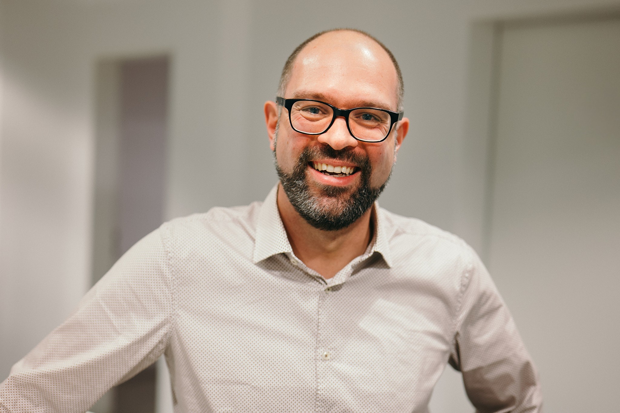 Ein Mann mit Bart und Brille, der ein helles Hemd trägt, lächelt, während er in einem hell beleuchteten Raum steht. Er arbeitet als Business Developm Manager.